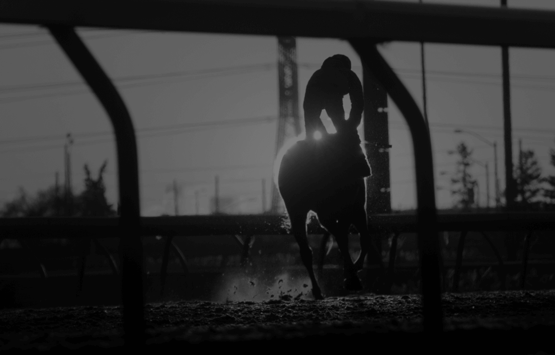 Silhouette of a jockey riding a horse on a racetrack at sunrise